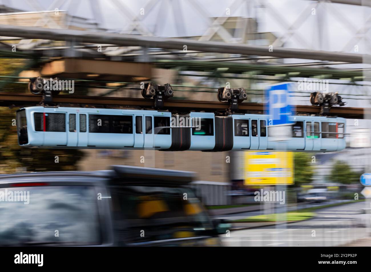 Wuppertal, Deutschland. September 2024. Eine Schwebebahn führt über eine Straße. Laut Marco Polo Trendguide`25 entwickelt sich die Stadt im Bergischen Land derzeit zu einer Art Kunsthochburg: „Wenn man in Wuppertal unterwegs ist, glaubt man seinen Augen nicht. Hyper-realistische, poetische, surreale und abstrakte Wandmalereien prangen meterhoch an den Fassaden.“ Sie sind Teil des Projekts Urbaner Kunstraum Wuppertal (UKW), das bis Ende 2025 mit 24 großformatigen Gemälden Farbe in die Stadtteile bringen wird. Quelle: Rolf Vennenbernd/dpa/Alamy Live News Stockfoto